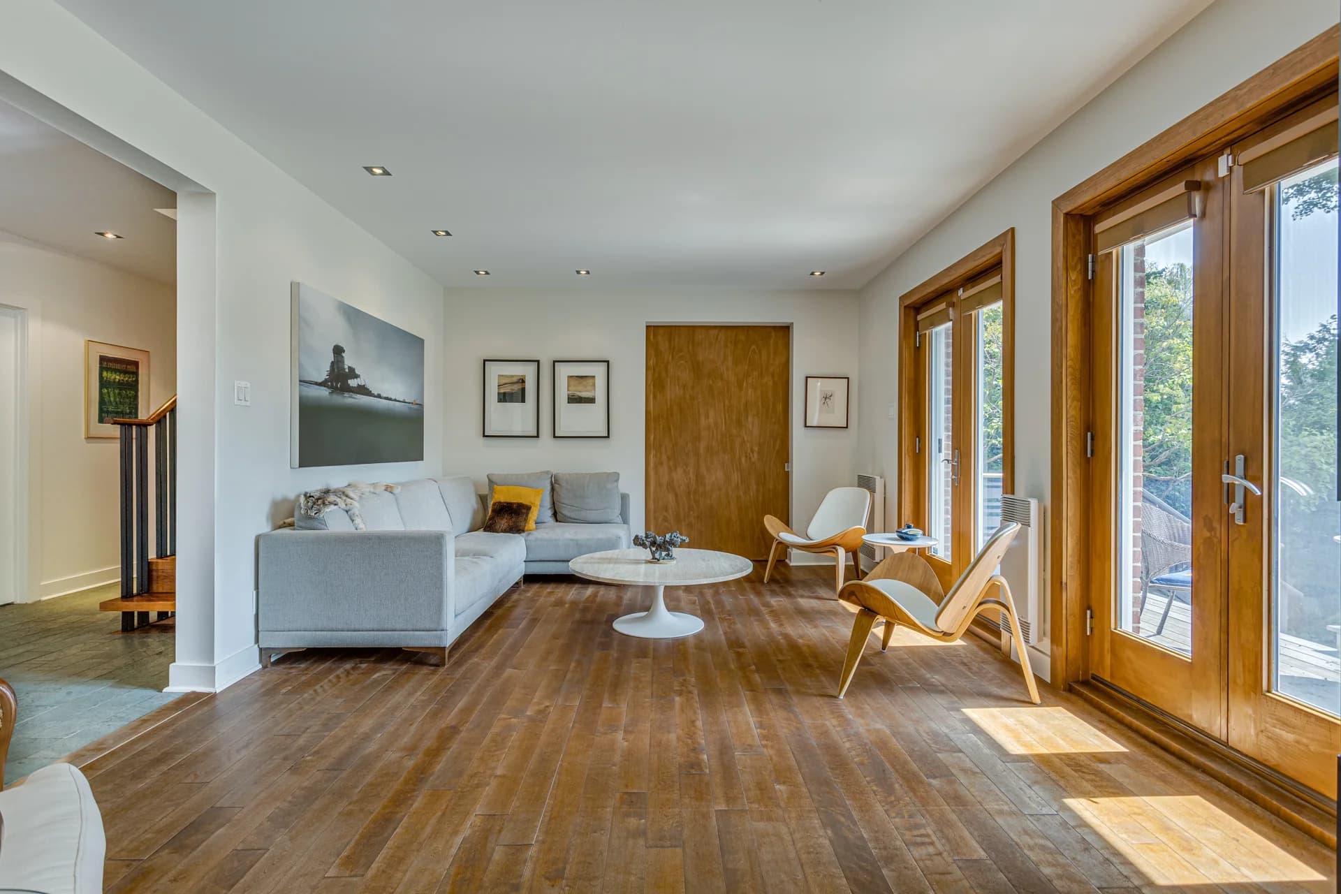 Salon clair avec plancher de bois et fenêtres donnant sur le jardin