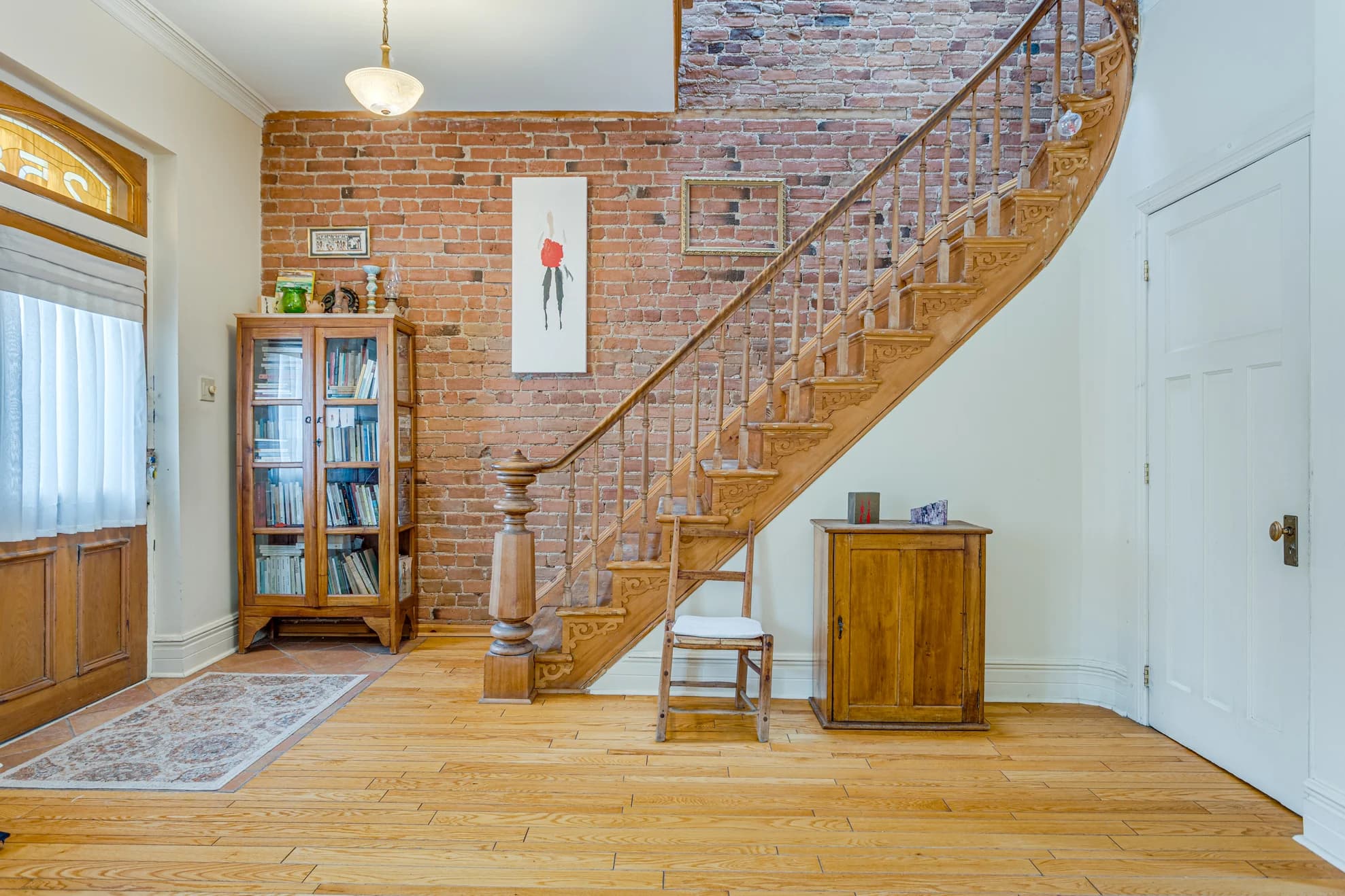 Entrée avec escalier courbe en bois et mur de brique