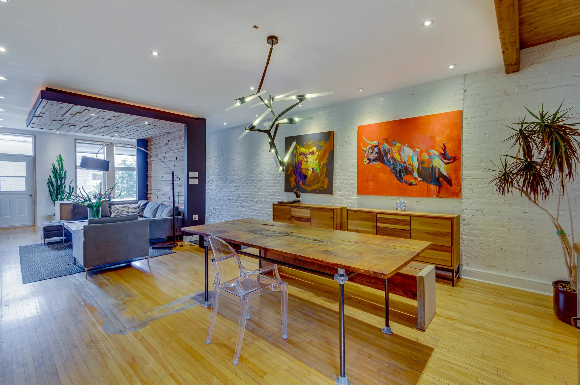 Salle à manger avec table en verre, œuvres colorées et mur de pierre